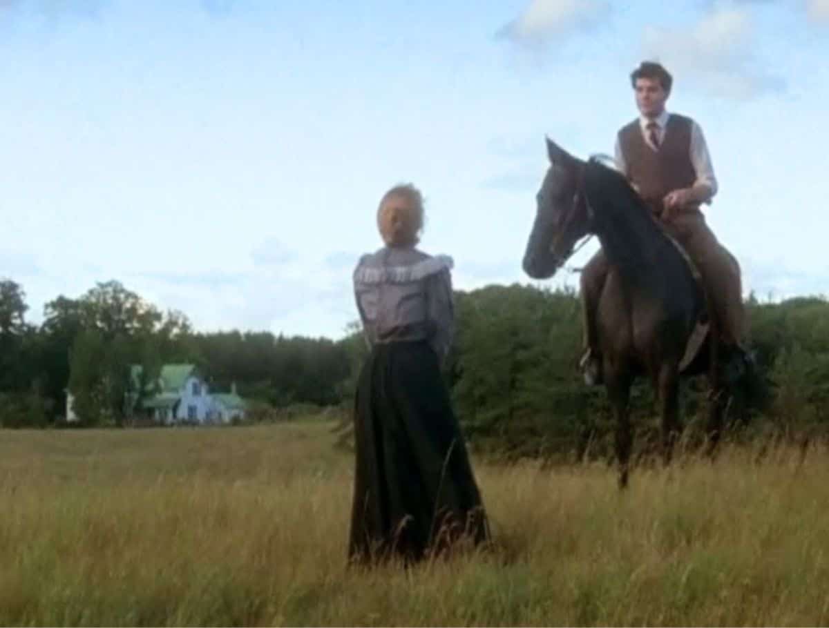 Field scene from Anne of Green Gables with anne standing with back to camera and gilbert on horse. green gables house can be seen in background