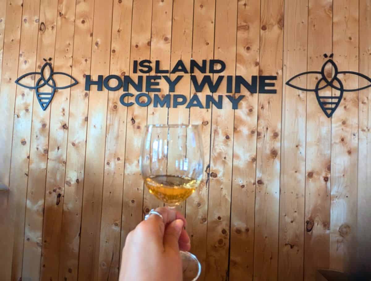 glass of Mead sampling in front of sign at Island Honey Wine Co