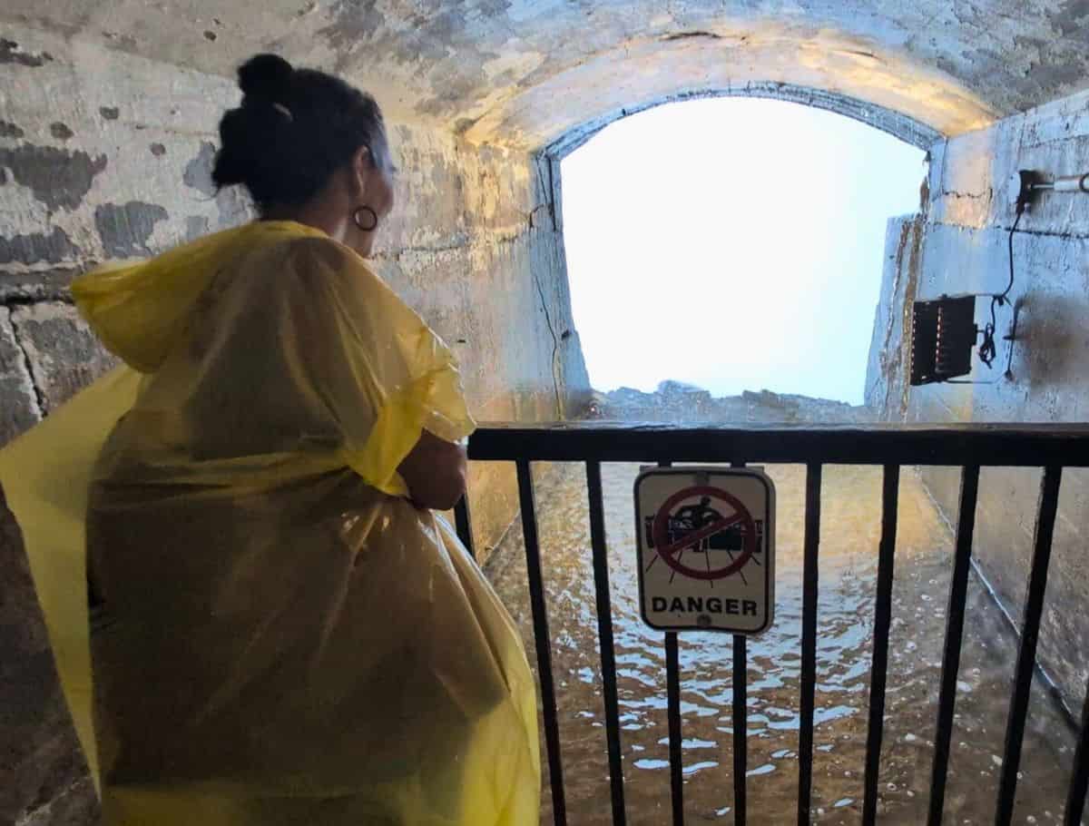 yellow ponchoed person standing at the Gated off section to see "behind the falls" (that wall of white at the opening)