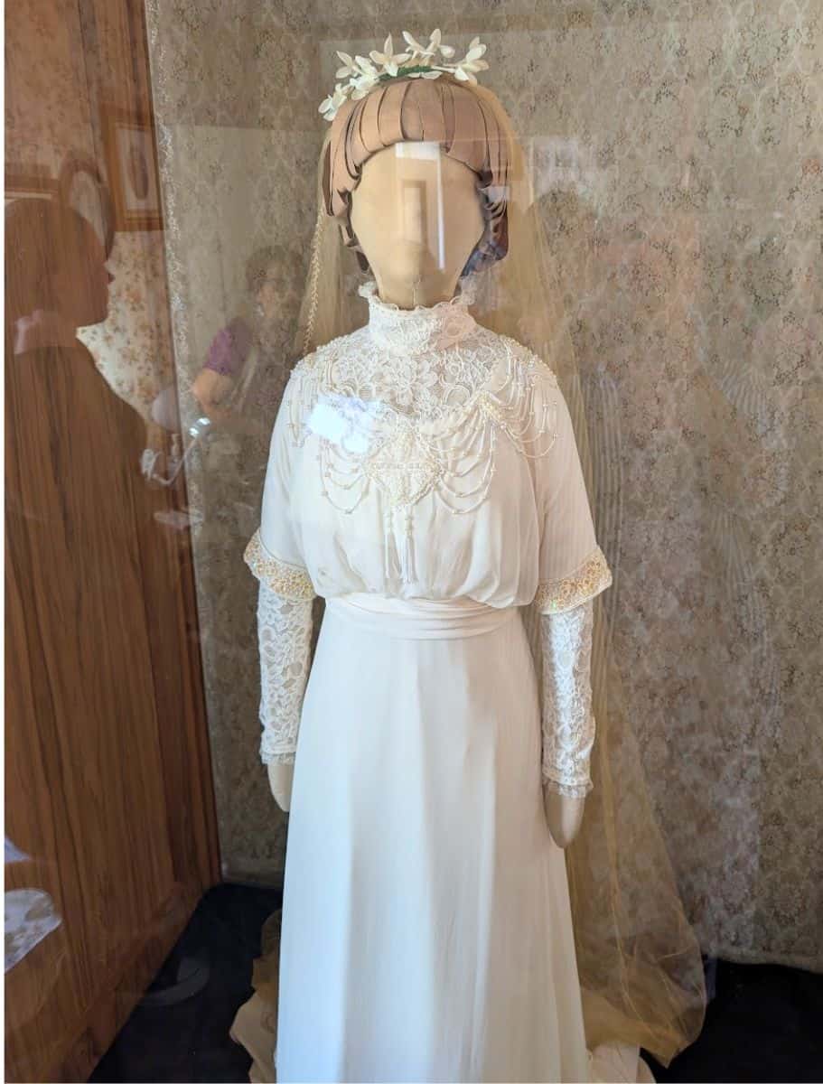 Accurate replica of L.M. Montgomery's wedding dress with lace and beadwork behind glass