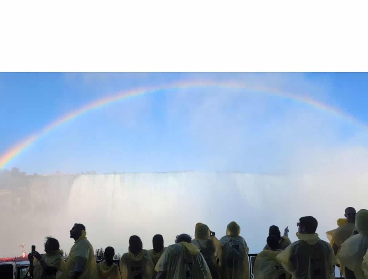 Full arch of a rainbow over Niagara Falls with yellow ponchoed onlookers