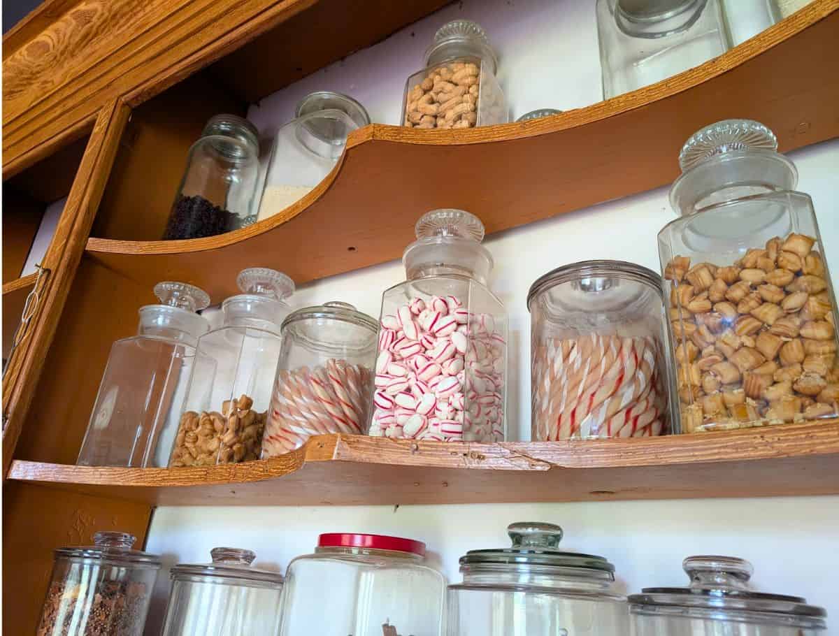 shelves with clear cannisters of candies, two of them with melted candy cane sticks that are actually over 100yrs old