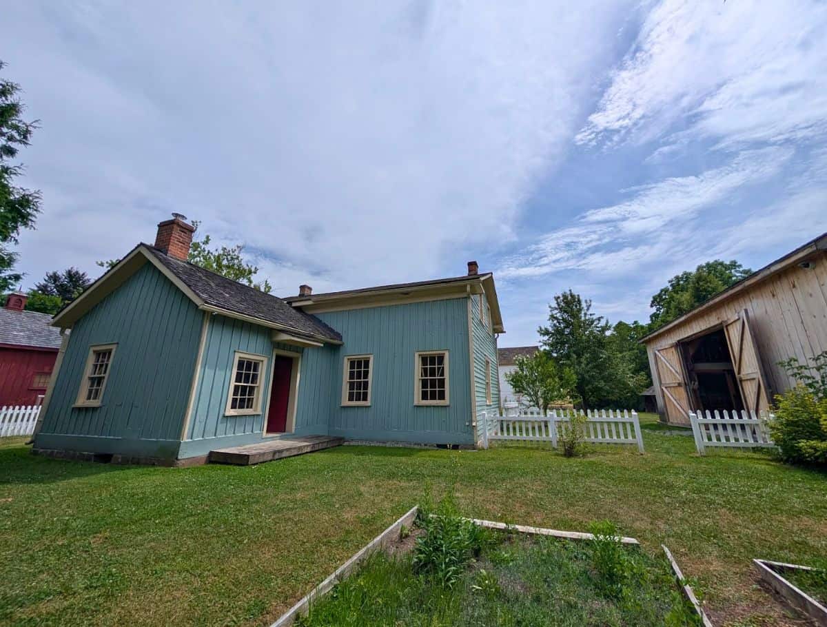 blue house with white picket fence and barn to the left