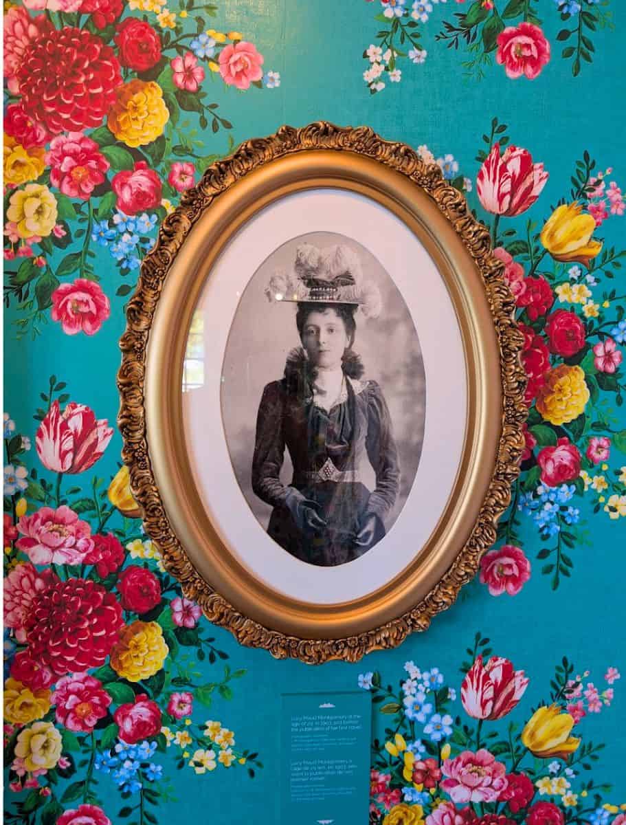 Portrait photo of L.M. Montgomery at post office museum with colorful flowers and bright teal wallpaper