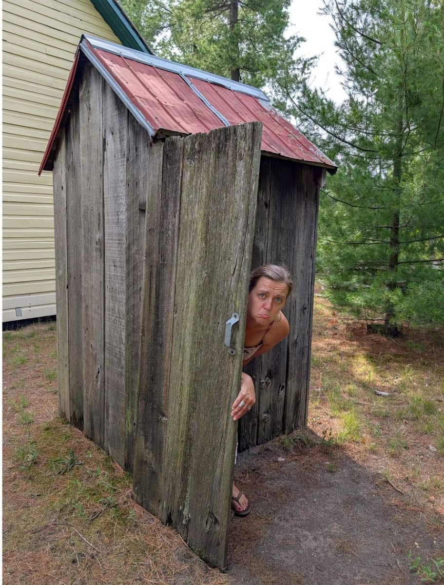 me peaking around the door of the outhouse behind the schoolhouse at simcoe county museum, the one used as the outhouse scene in anne of avonlea