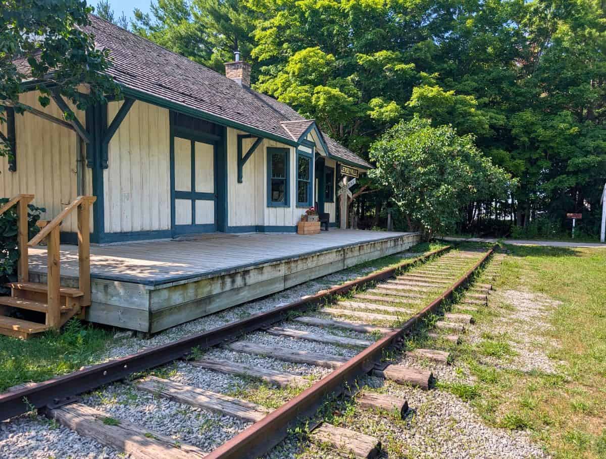 white and green Jerseyville Train Station at Westfield Heritage Museum with railtrack running in front of it into the forest
