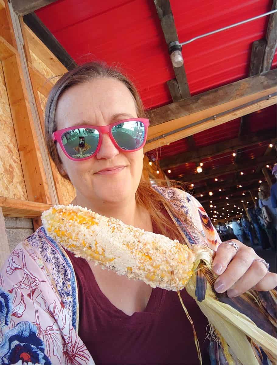 selfie of me with fresh grilled corn on stick with mexican cheese covering it