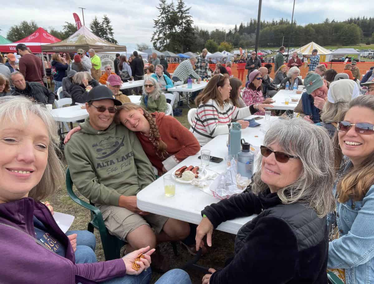 group of people taking a selfie at the crowded ciderfest with vendor tents in background