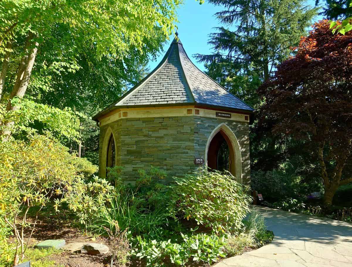 Small stone garden structure with a pointed roof sits along a winding path surrounded by lush greenery and trees in a peaceful park setting. Wandering through tranquil gardens like this is one of the quieter things to do Whidbey Island visitors can enjoy.